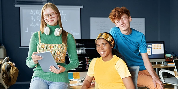 Drei Jugendliche in einem modernen Klassenraum mit digitalen Geräten – Symbol für Talentförderung und Zukunftskompetenz.