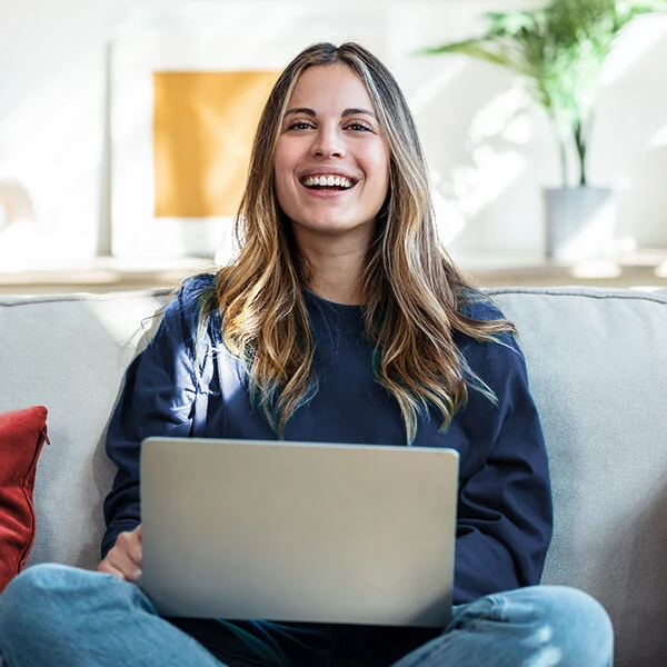 Junge Frau arbeitet lächelnd mit Laptop von zu Hause aus – Symbol für Flexibilität, Work-Life-Balance und moderne Arbeitsmodelle.