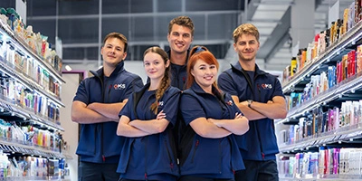 Fünf Mitarbeitende der OMS Retail Academy im Markt, stehend zwischen Regalen mit Drogerieartikeln – stellvertretend für das Team auf der Fläche.