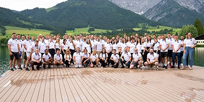Gruppenfoto eines internationalen Teams vor alpiner Kulisse – gemeinsames Offsite-Event am See.
