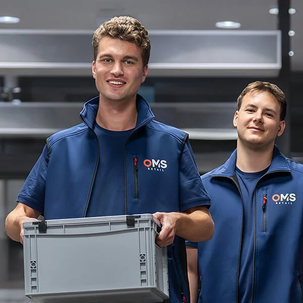 Zwei OMS-Retail Mitarbeiter tragen eine graue Transportkiste während einer Bestandesaufnahme im Einzelhandel