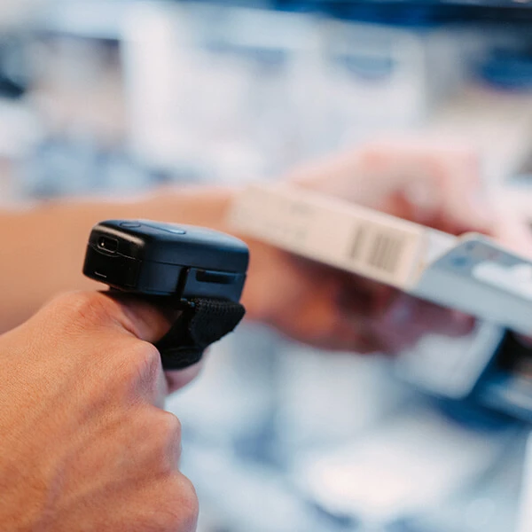 Hand hält ein mobiles Scangerät und erfasst den Barcode eines Produkts im Regal während der Inventur.