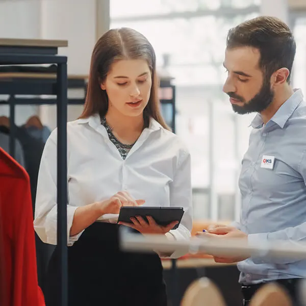 Eine Geschäftsfrau und ein OMS-Retail-Berater besprechen ein Inventurverfahren in einem Bekleidungsgeschäft.
